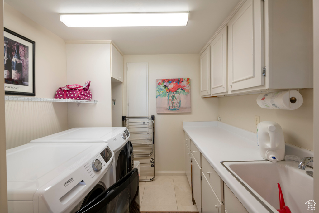 Clothes washing area with cabinets, sink, light tile patterned floors, and washing machine and clothes dryer