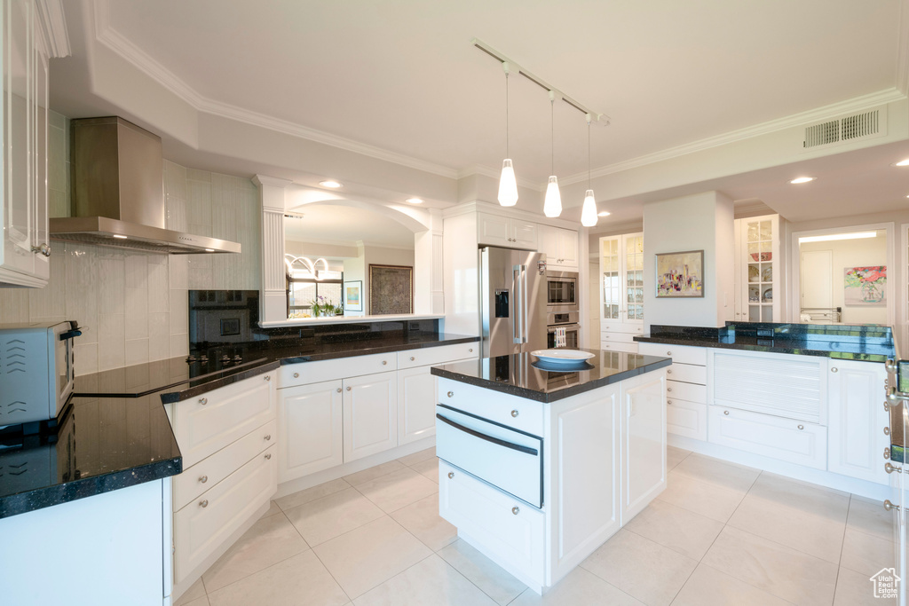 Kitchen featuring backsplash, wall chimney range hood, white cabinetry, appliances with stainless steel finishes, and a center island