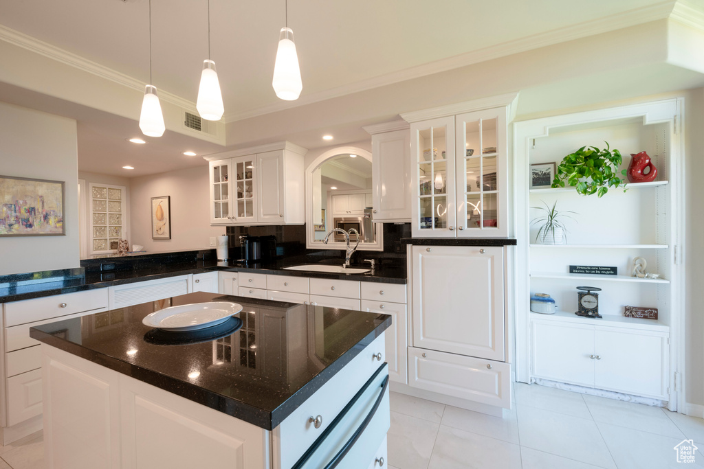 Kitchen featuring light tile patterned flooring, white cabinetry, a center island, decorative light fixtures, and sink