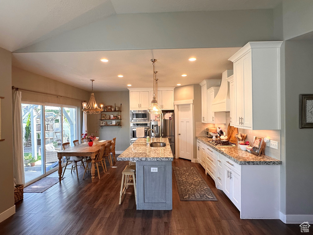 Kitchen featuring pendant lighting, lofted ceiling, a kitchen island with sink, white cabinetry, and custom range hood