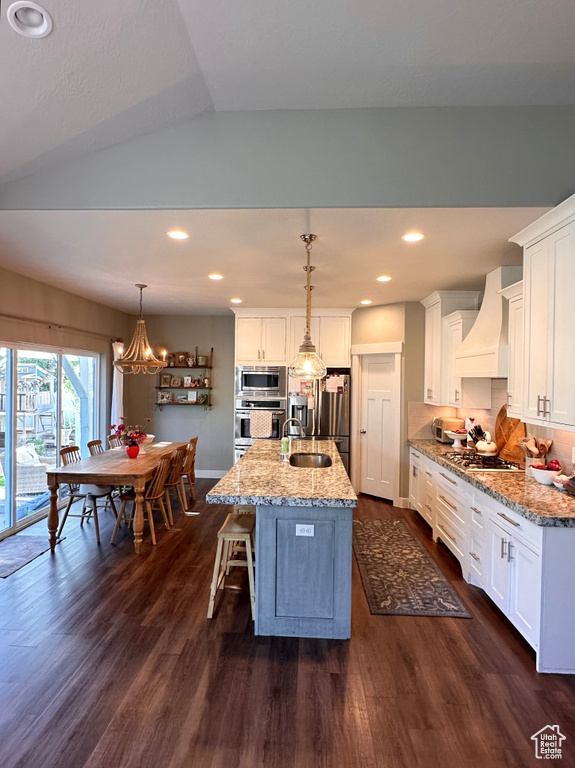 Kitchen with pendant lighting, white cabinets, vaulted ceiling, a center island with sink, and dark hardwood / wood-style flooring