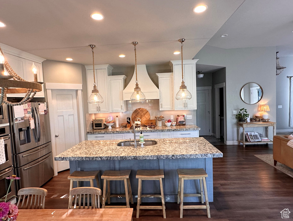 Kitchen with pendant lighting, light stone counters, a kitchen island with sink, white cabinetry, and stainless steel appliances