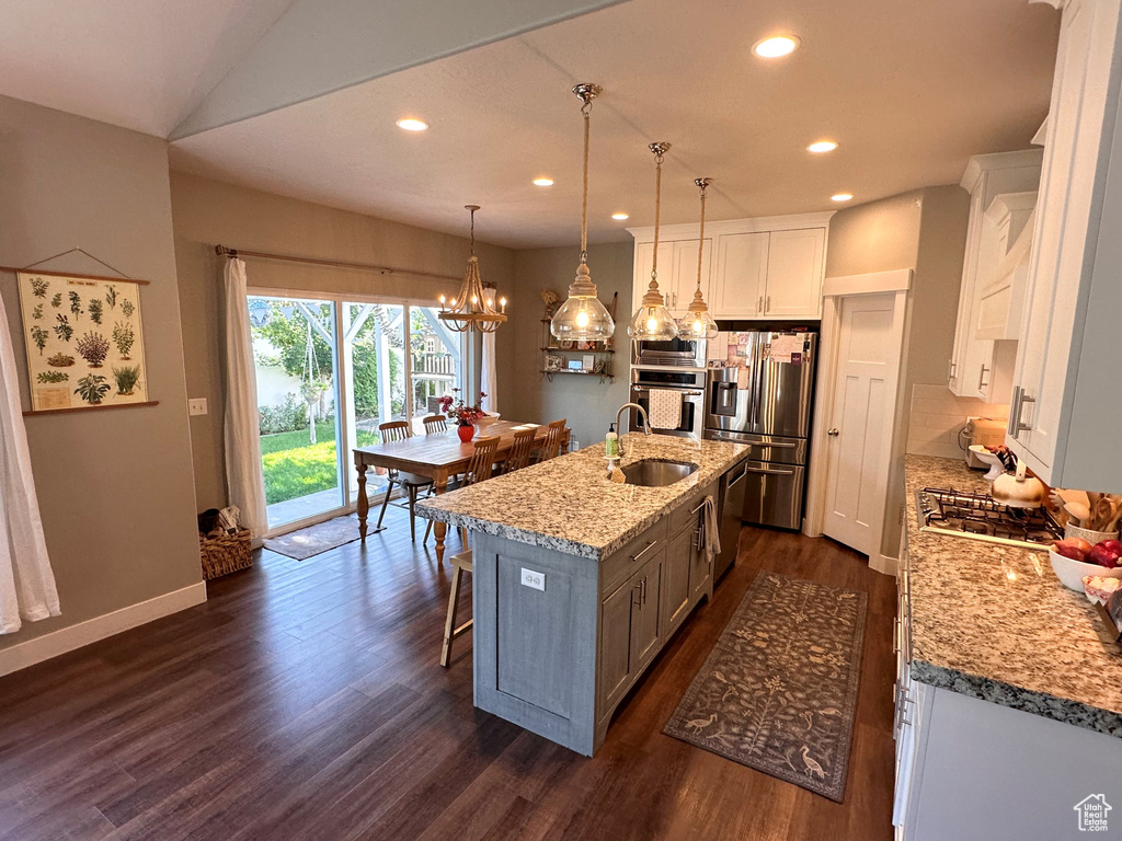 Kitchen featuring white cabinets, hanging light fixtures, a kitchen island with sink, stainless steel appliances, and light stone countertops