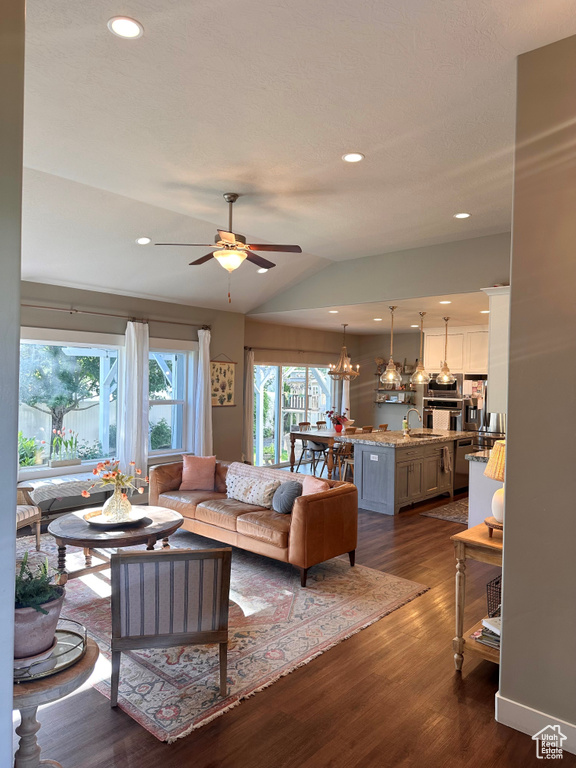 Living room with ceiling fan with notable chandelier, lofted ceiling, dark hardwood / wood-style flooring, and sink