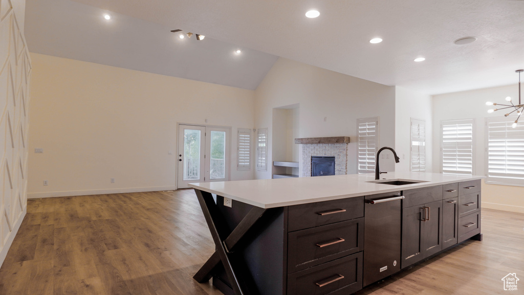 Kitchen with sink, stainless steel dishwasher, a kitchen island with sink, a notable chandelier, and a fireplace