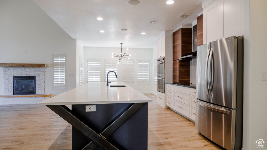 Kitchen featuring white cabinets, a kitchen island with sink, appliances with stainless steel finishes, and hanging light fixtures