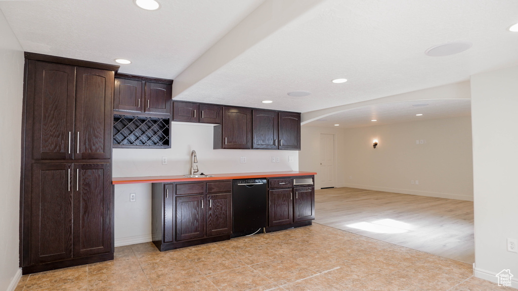 Kitchen with sink, dark brown cabinets, black dishwasher, light hardwood / wood-style floors, and decorative backsplash