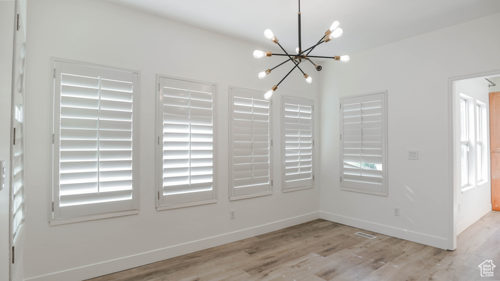 Unfurnished dining area featuring an inviting chandelier, light hardwood / wood-style floors, and a wealth of natural light