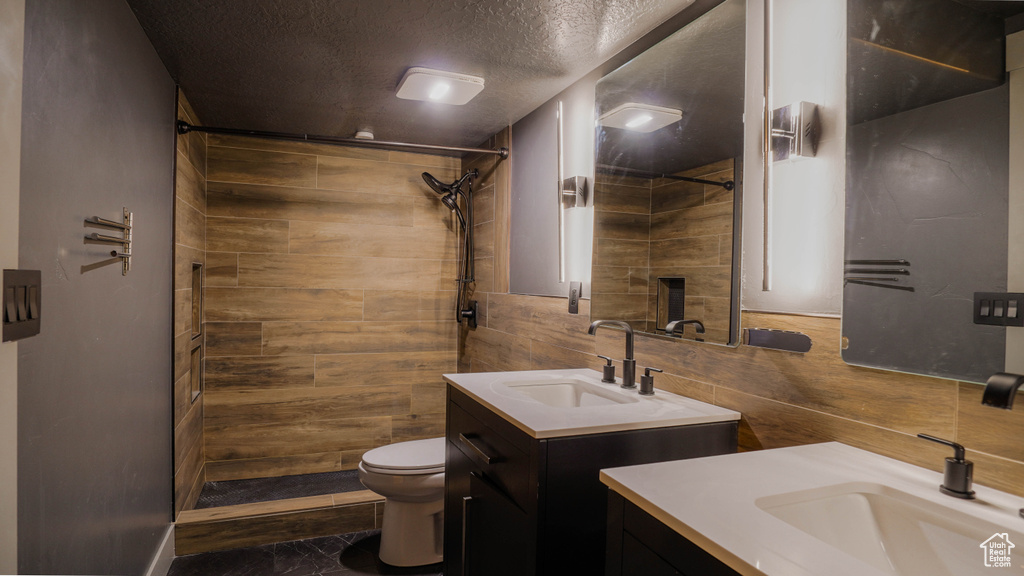 Bathroom featuring vanity, toilet, a textured ceiling, and tiled shower