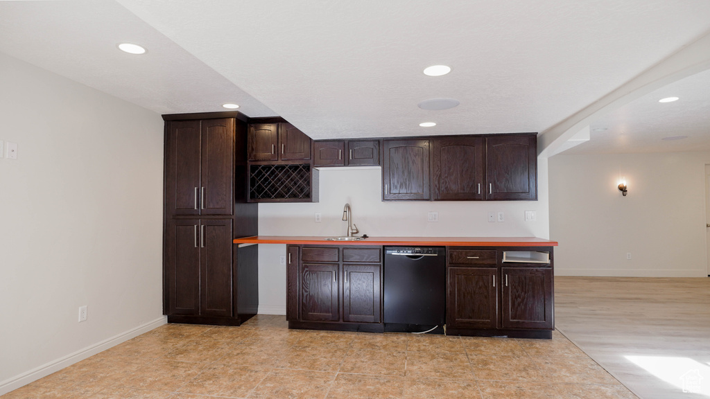 Kitchen featuring dark brown cabinetry, black dishwasher, sink, and wood counters