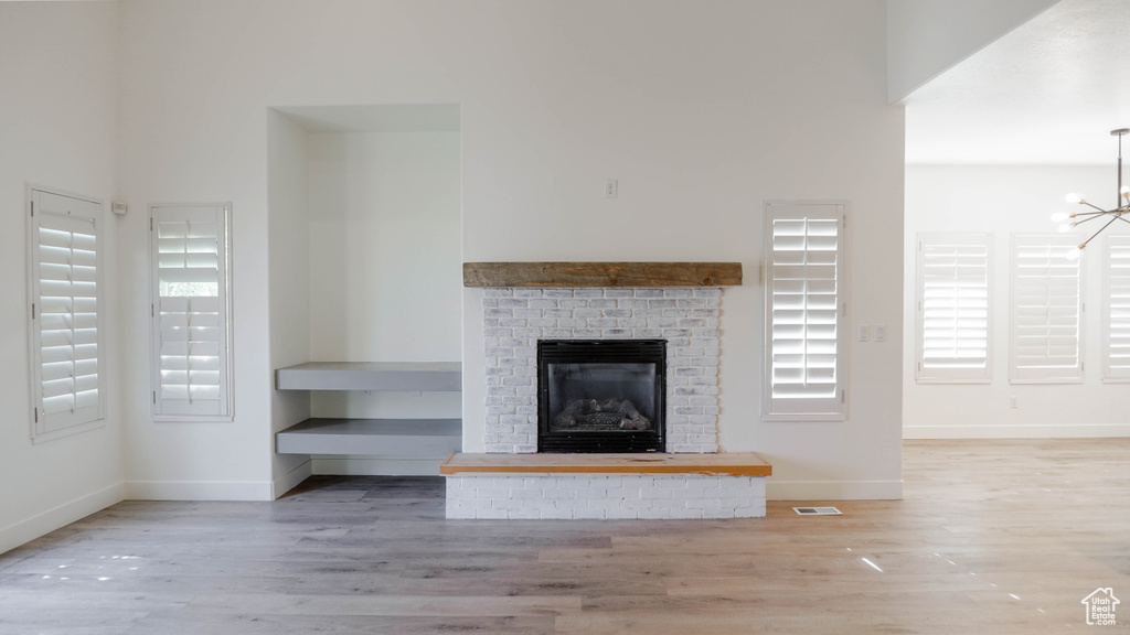 Unfurnished living room featuring a healthy amount of sunlight, a fireplace, hardwood / wood-style floors, and a notable chandelier