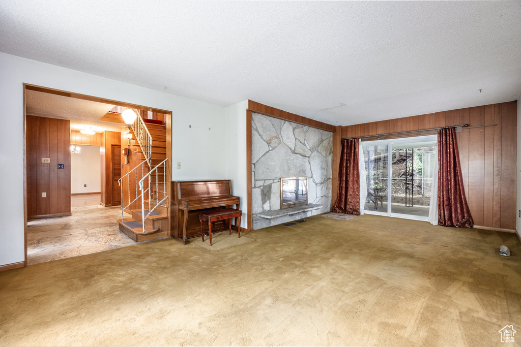 Carpeted living room with a textured ceiling, a fireplace, and wood walls