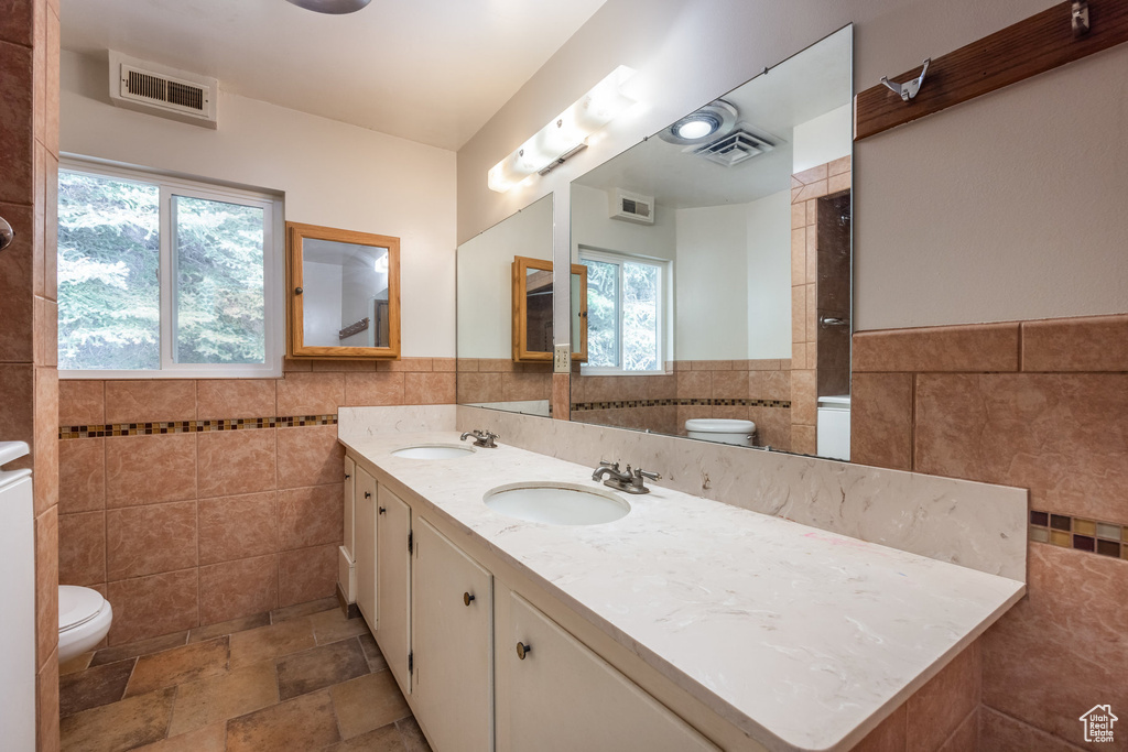 Bathroom featuring a healthy amount of sunlight, tile walls, vanity, and toilet