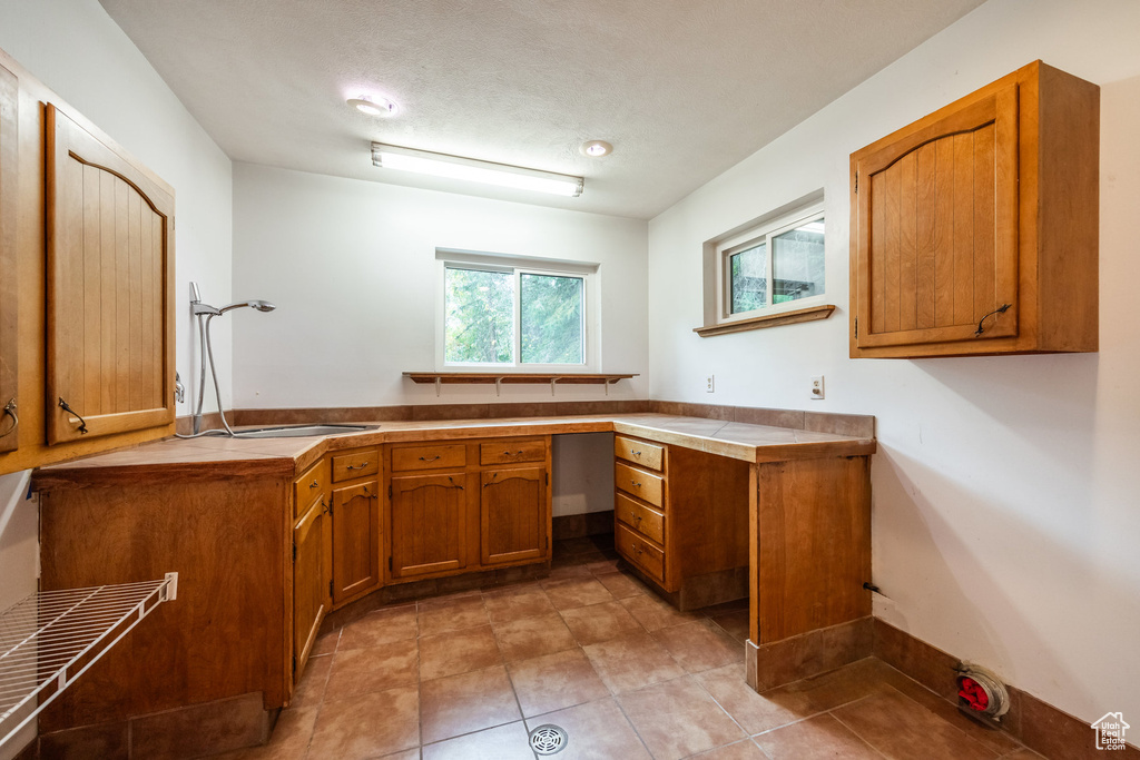 Kitchen featuring built in desk, kitchen peninsula, light tile patterned flooring, and a textured ceiling