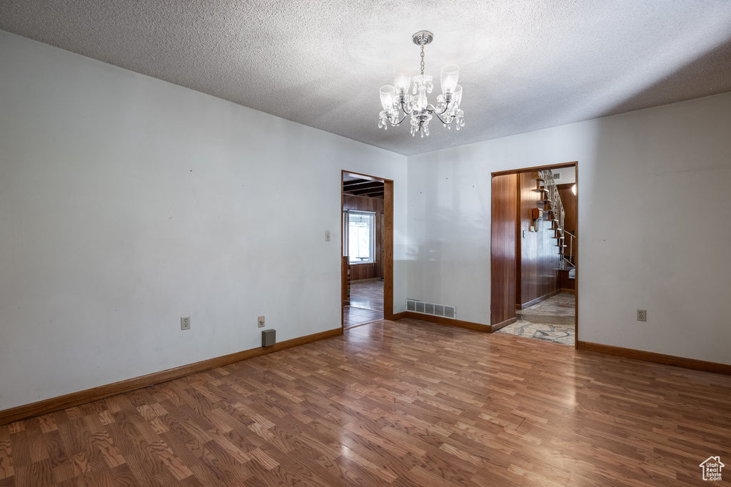 Empty room with wood-type flooring, a chandelier, and a textured ceiling