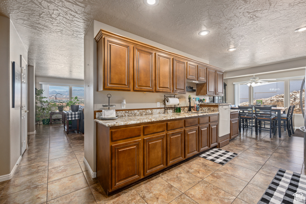 Kitchen with a textured ceiling, light tile patterned flooring, ceiling fan, and light stone counters