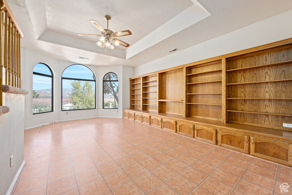 Unfurnished living room featuring ceiling fan, a raised ceiling, light tile patterned flooring, and a textured ceiling