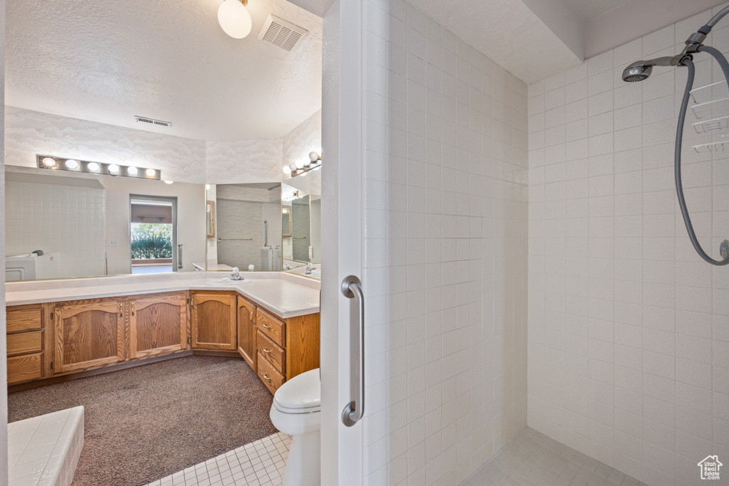 Bathroom featuring vanity, toilet, a textured ceiling, and tiled shower