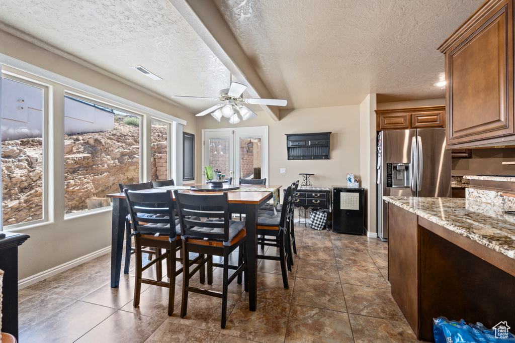 Dining space featuring a textured ceiling, beamed ceiling, ceiling fan, and dark tile patterned flooring