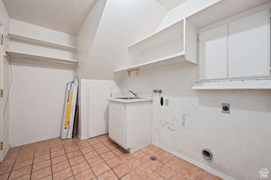 Laundry area featuring cabinets, light tile patterned flooring, a textured ceiling, and electric dryer hookup