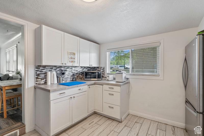 Kitchen with a textured ceiling, appliances with stainless steel finishes, and white cabinetry