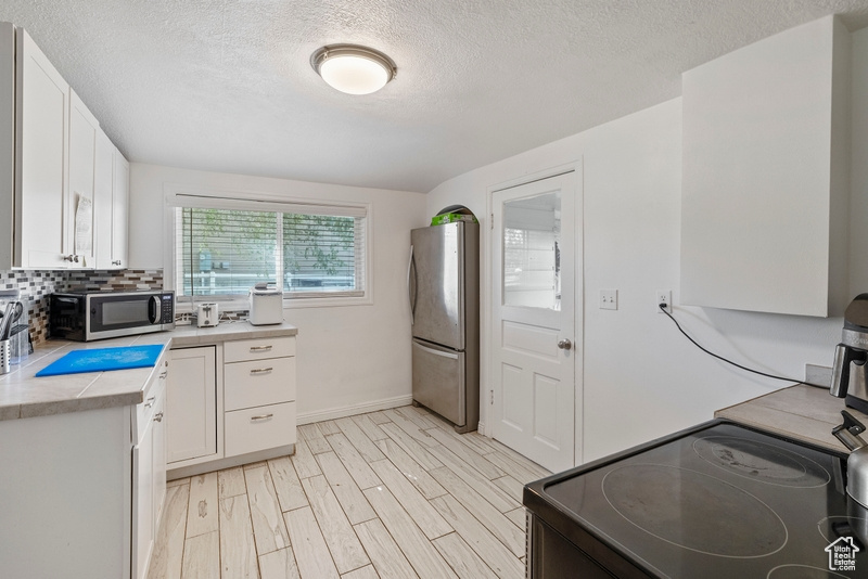 Kitchen with a textured ceiling, decorative backsplash, white cabinetry, and stainless steel appliances