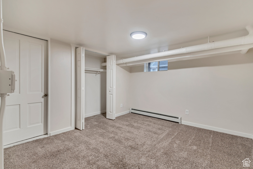 Unfurnished bedroom with light carpet and a baseboard heating unit