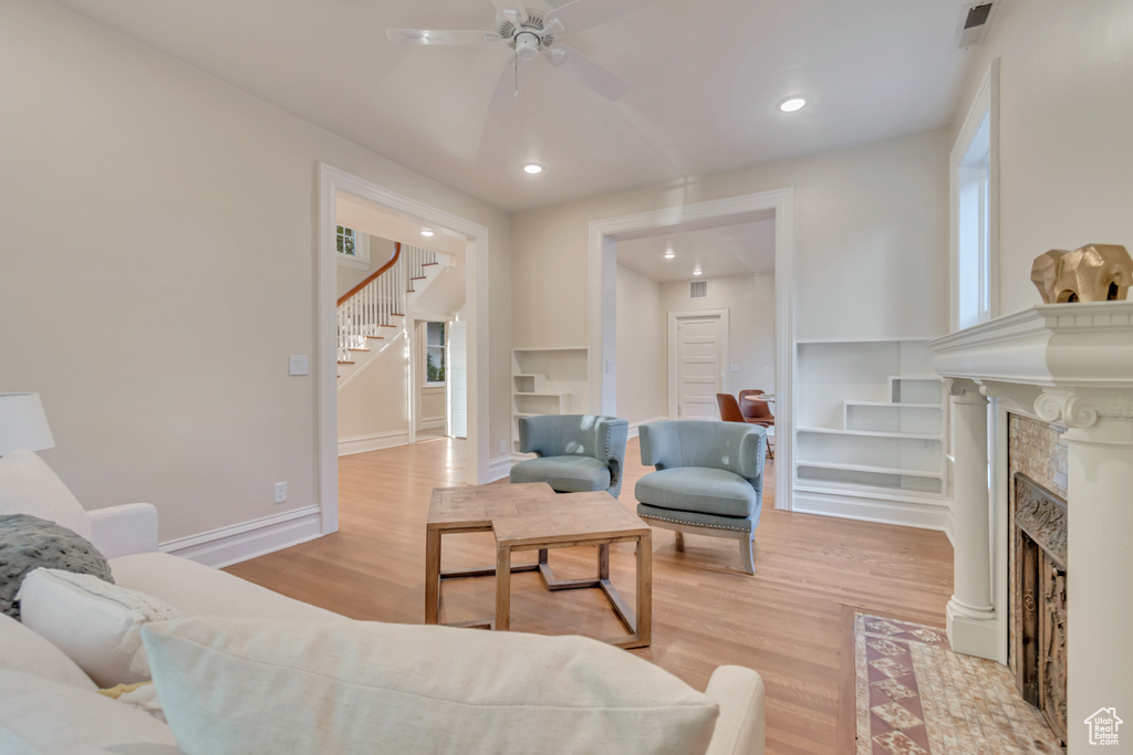 Living room with a fireplace, ceiling fan, and light hardwood / wood-style flooring