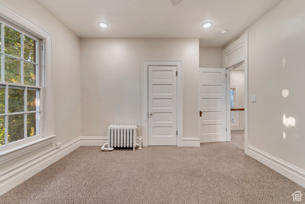 Interior space featuring a healthy amount of sunlight, radiator, and light carpet