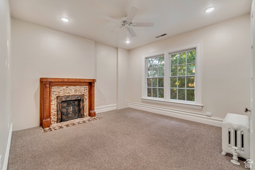 Unfurnished living room featuring ceiling fan, carpet flooring, and radiator heating unit