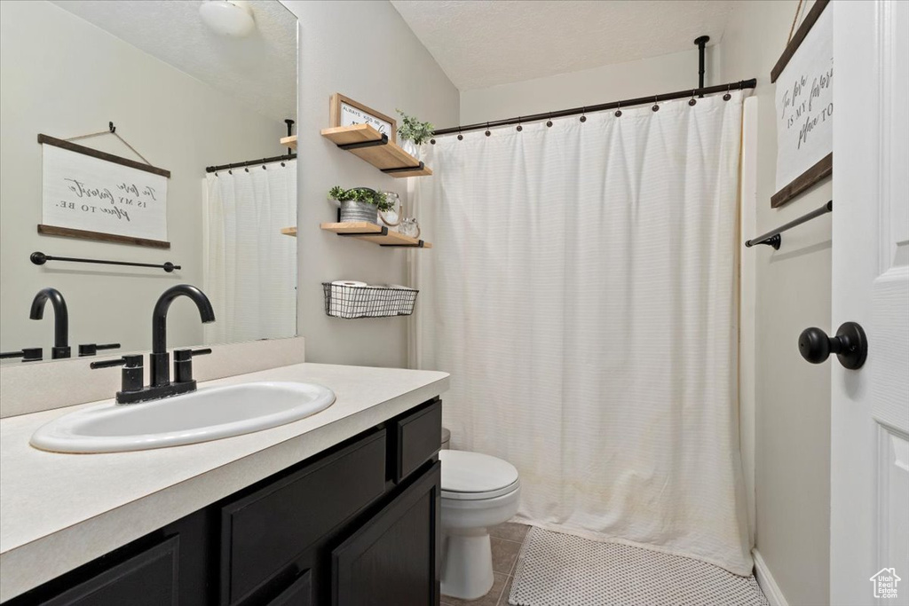 Bathroom featuring tile patterned flooring, a textured ceiling, toilet, vanity, and curtained shower