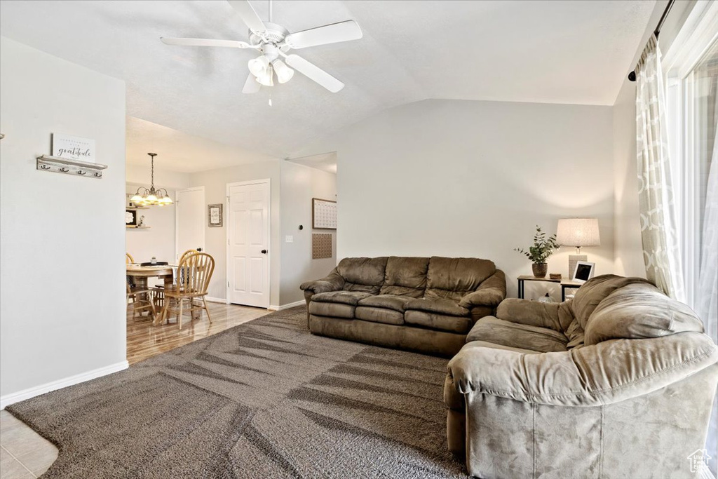 Living room with ceiling fan with notable chandelier, vaulted ceiling, and light hardwood / wood-style flooring