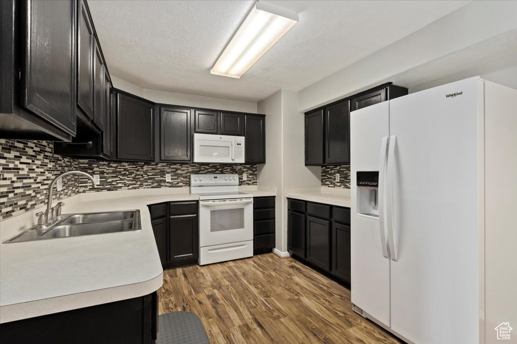 Kitchen with a textured ceiling, hardwood / wood-style flooring, sink, decorative backsplash, and white appliances