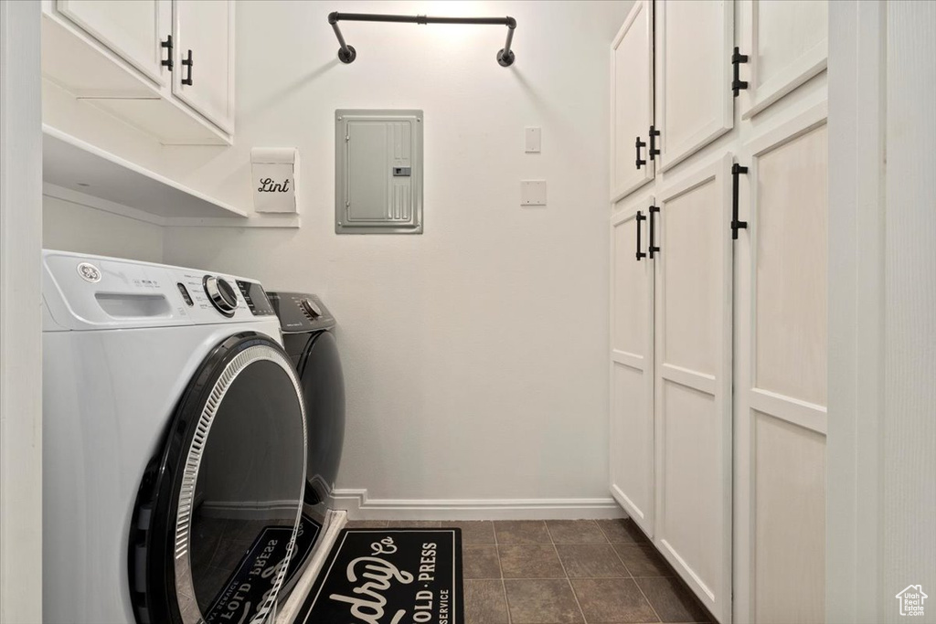 Clothes washing area with washer and clothes dryer, electric panel, dark tile patterned flooring, and cabinets