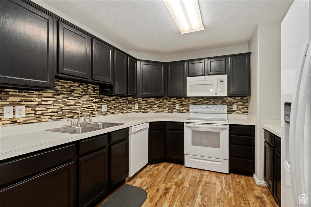 Kitchen featuring tasteful backsplash, white appliances, light wood-type flooring, a textured ceiling, and sink