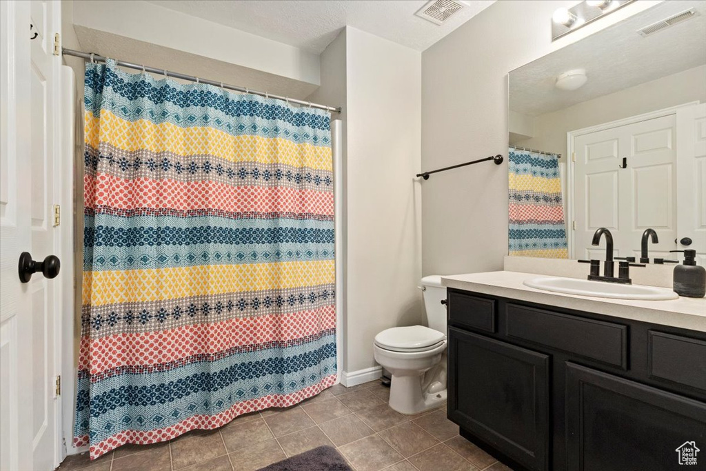 Bathroom with a textured ceiling, walk in shower, tile patterned floors, vanity, and toilet