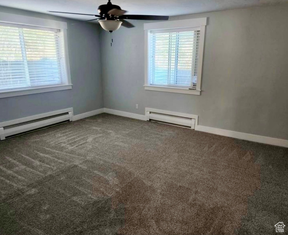 Carpeted spare room with baseboard heating, ceiling fan, and plenty of natural light