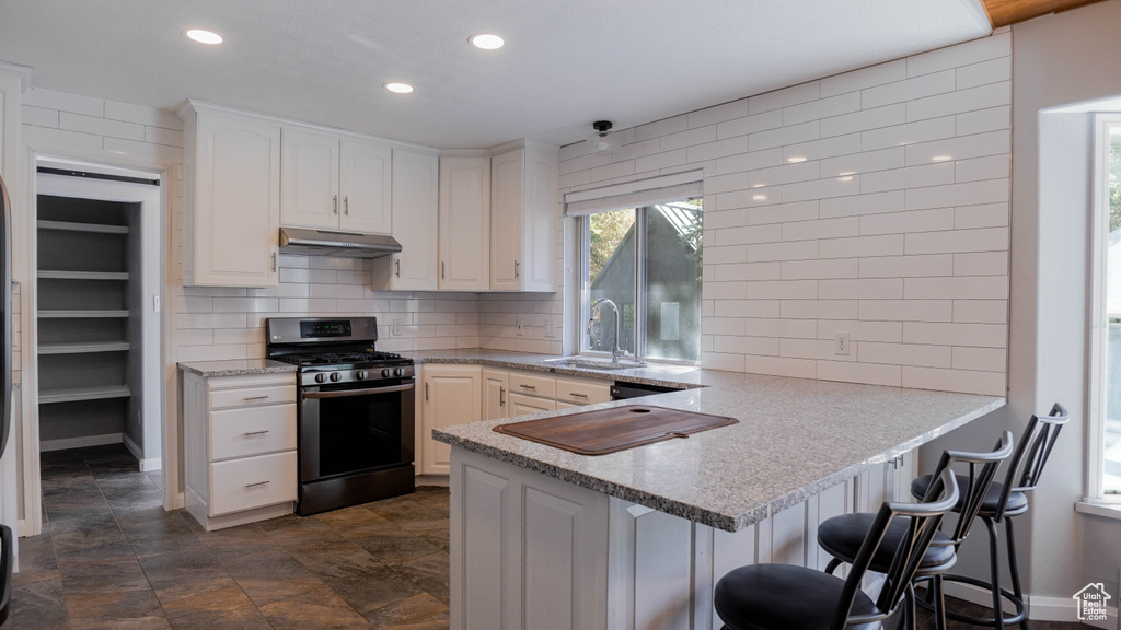 Kitchen featuring white cabinets, sink, kitchen peninsula, a kitchen breakfast bar, and stainless steel range with gas cooktop