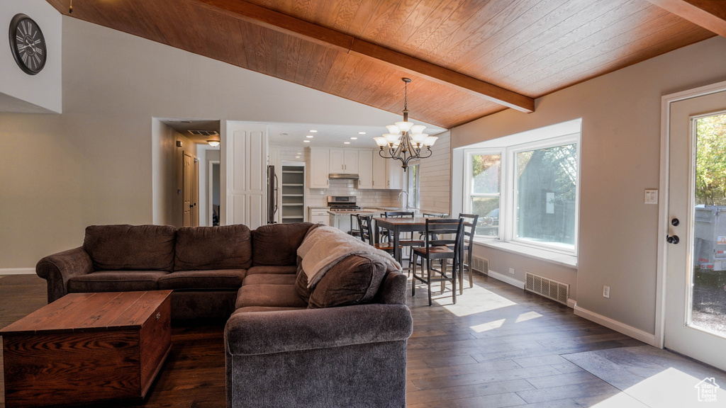 Living room with a notable chandelier, a wealth of natural light, vaulted ceiling with beams, and dark hardwood / wood-style flooring