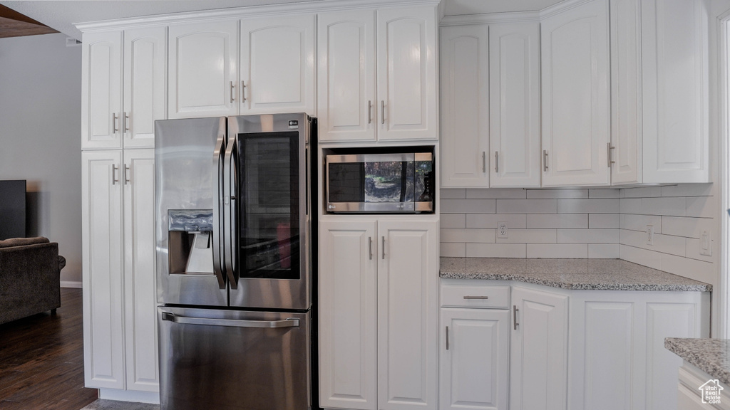 Kitchen featuring dark hardwood / wood-style floors, tasteful backsplash, white cabinetry, stainless steel appliances, and light stone countertops