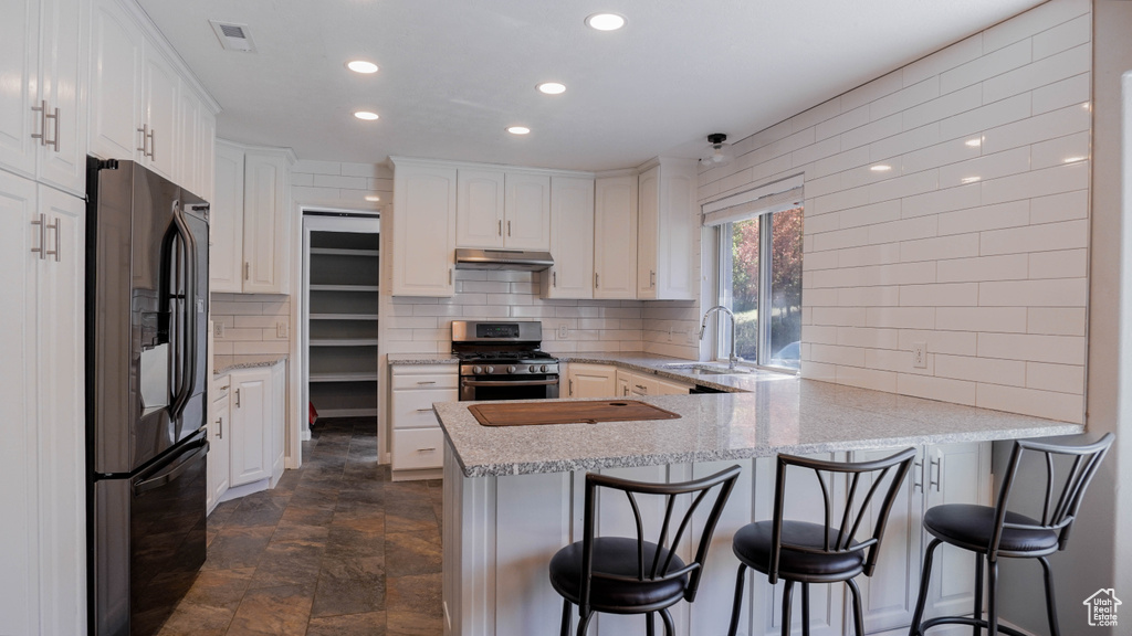 Kitchen with sink, kitchen peninsula, white cabinetry, stainless steel appliances, and a breakfast bar area