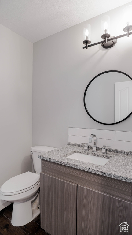 Bathroom with a textured ceiling, hardwood / wood-style flooring, vanity, and toilet