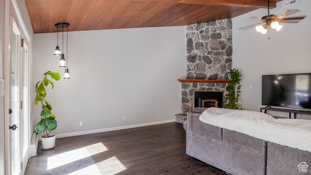 Living room featuring ceiling fan, a stone fireplace, lofted ceiling with beams, dark hardwood / wood-style floors, and wooden ceiling