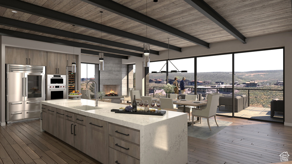 Kitchen with beam ceiling, hanging light fixtures, a fireplace, a center island with sink, and hardwood / wood-style floors