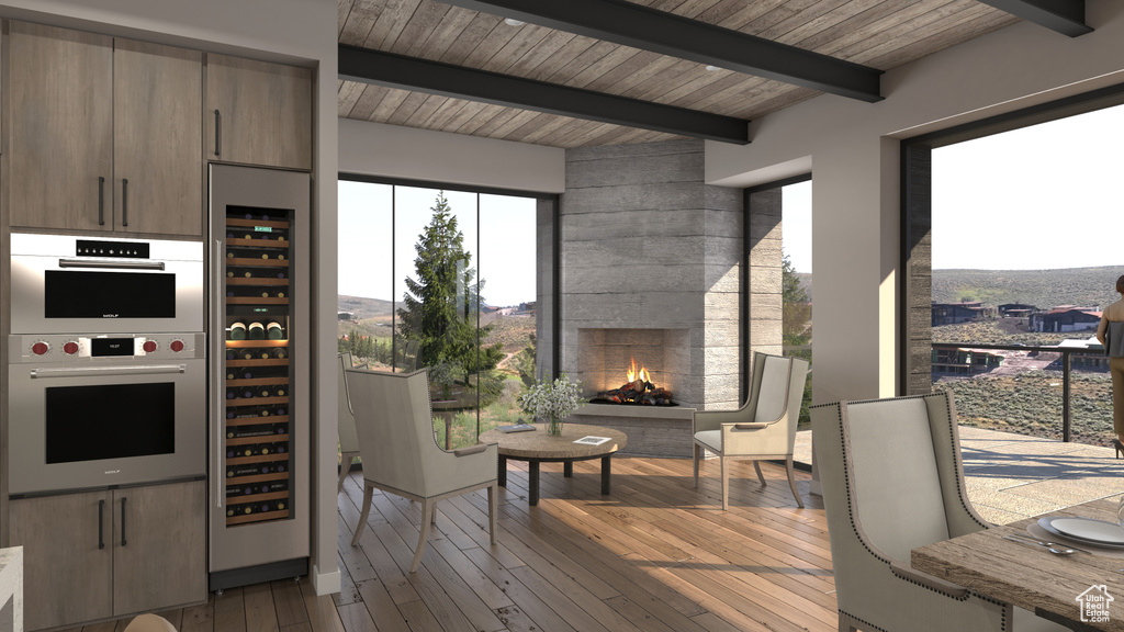 Kitchen with light hardwood / wood-style floors, beamed ceiling, beverage cooler, stainless steel double oven, and a fireplace