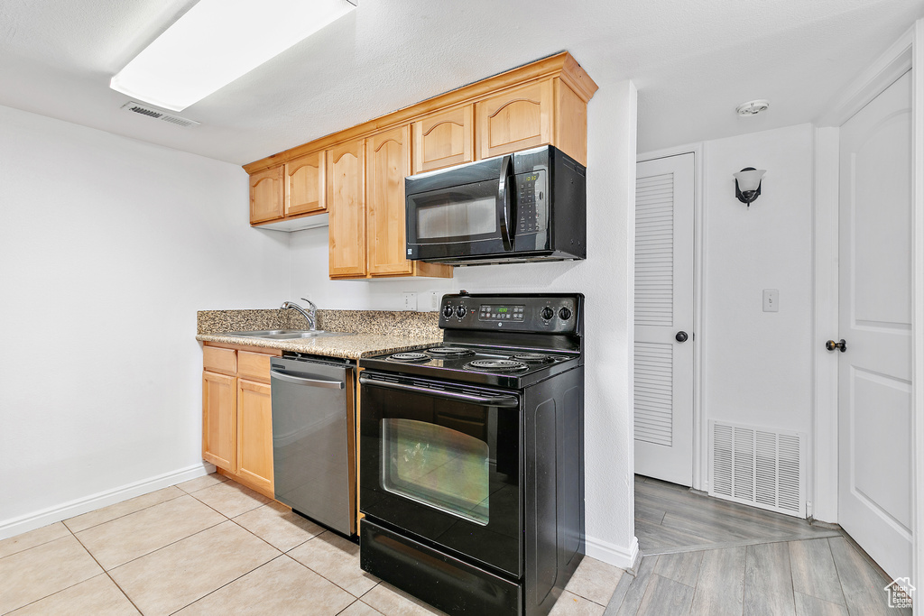 Kitchen with light hardwood / wood-style flooring, black appliances, light brown cabinetry, and sink