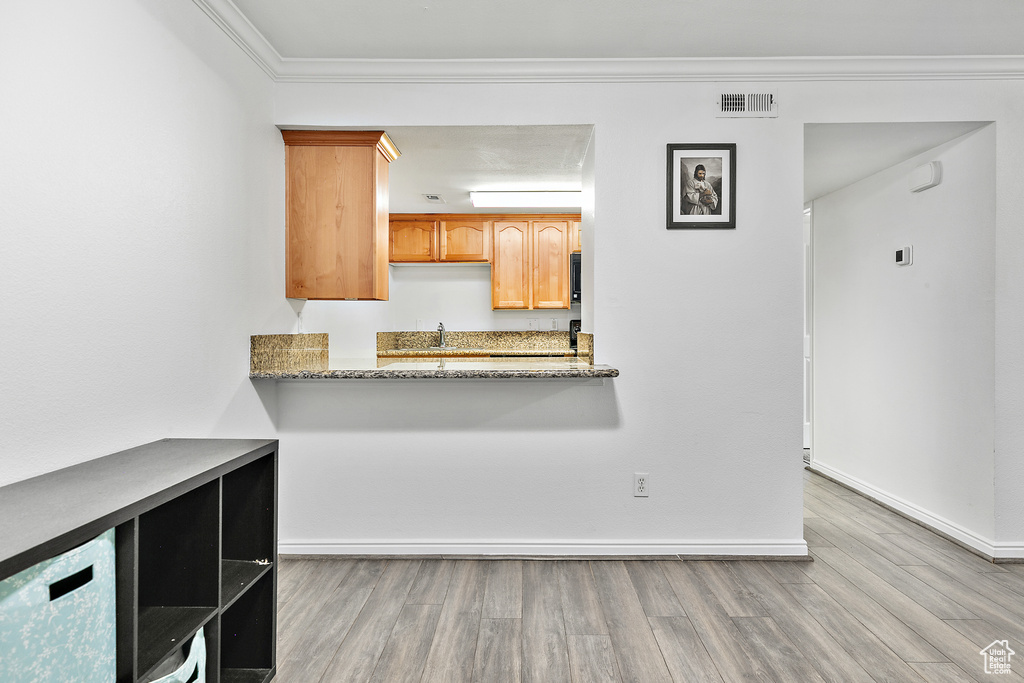 Kitchen with light wood-type flooring, crown molding, sink, and light stone counters