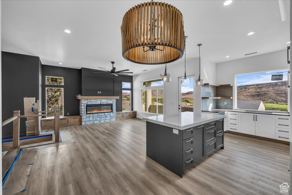 Kitchen with ceiling fan, hanging light fixtures, a kitchen island, a stone fireplace, and white cabinetry