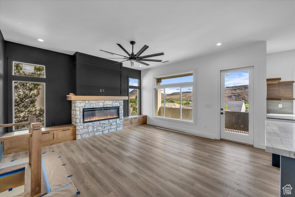 Unfurnished living room with wood-type flooring, ceiling fan, and a stone fireplace