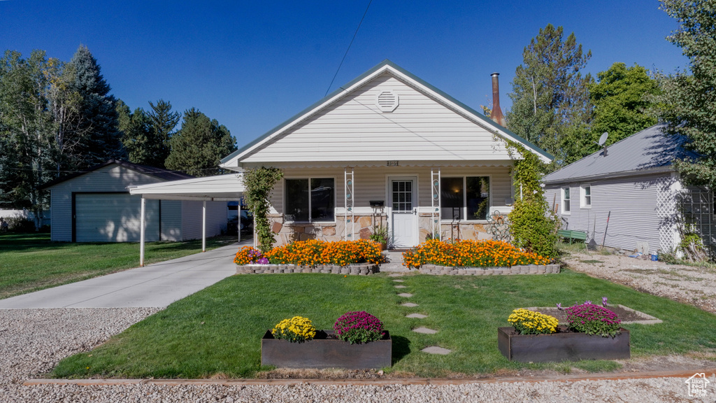 Bungalow featuring a front lawn, a carport, covered porch, and an outbuilding